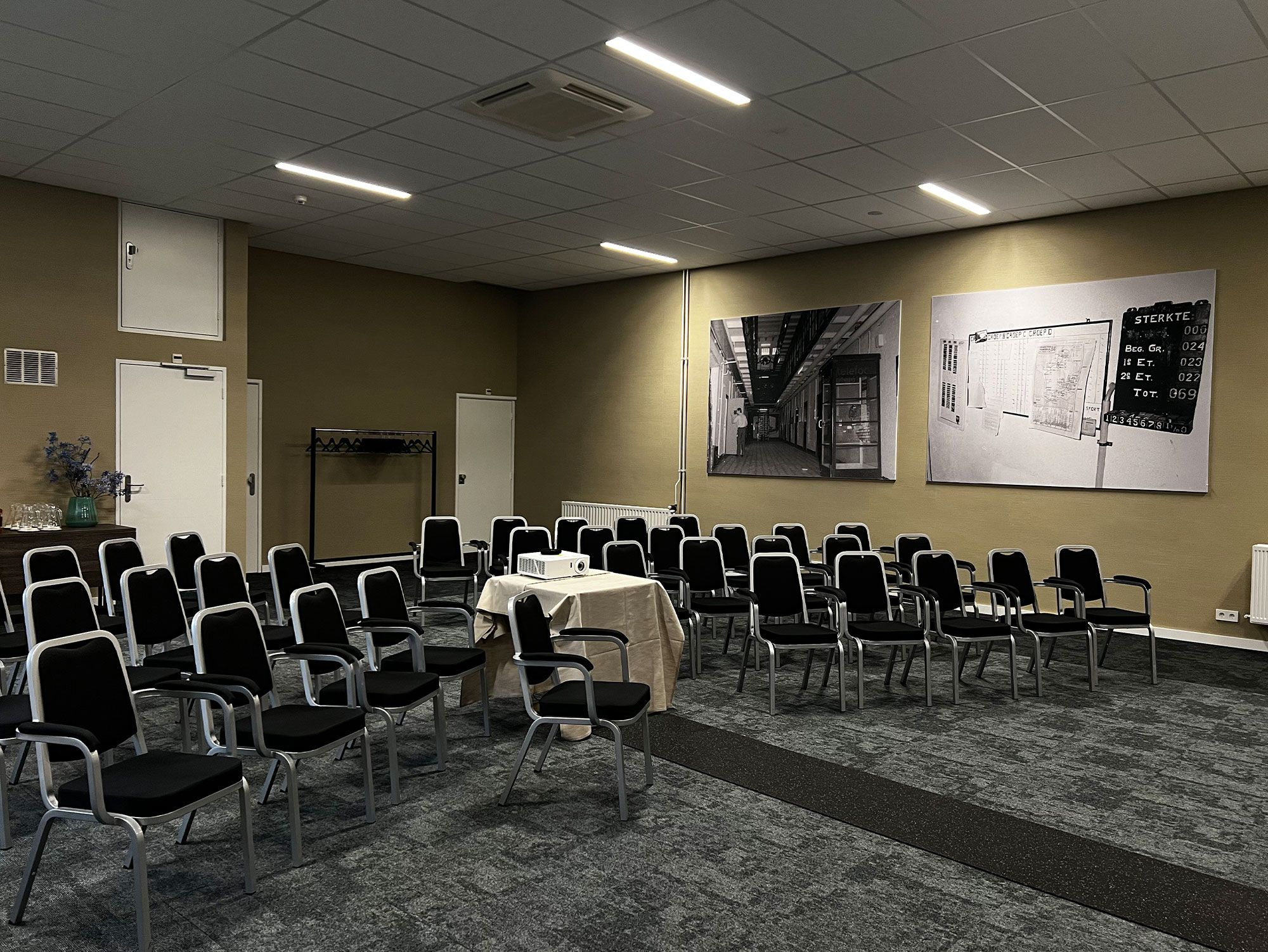 Un salón de conferencias con filas de sillas, un proyector y una mesa.