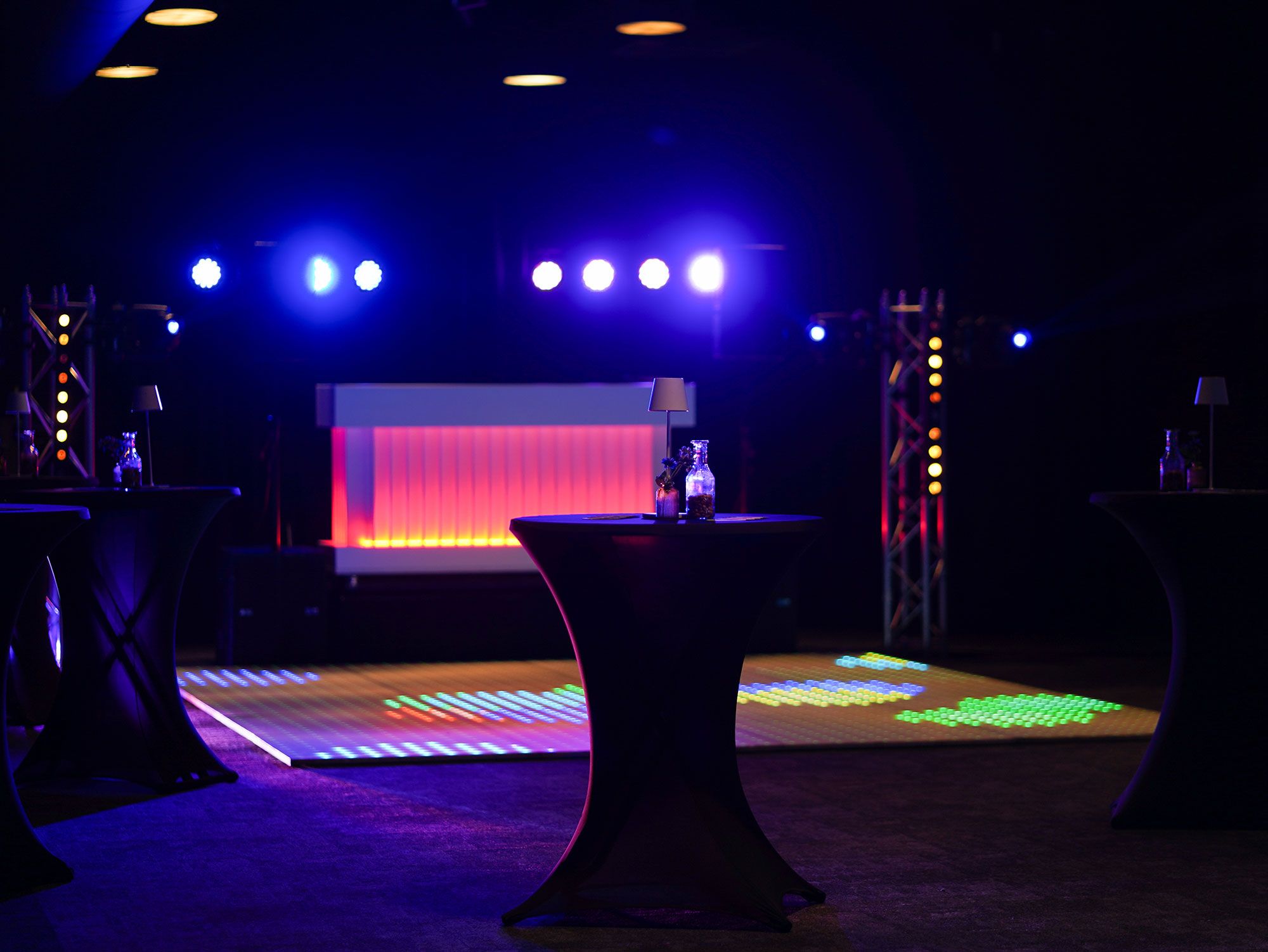 A stage with a red backdrop and a table with a bottle in the foreground.