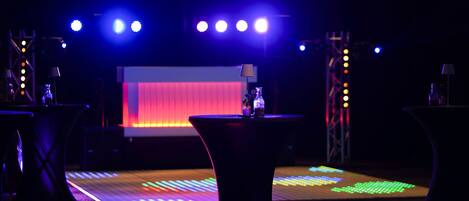 A stage with a red backdrop and a table with a bottle in the foreground.