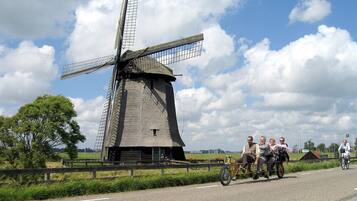En vindmølle ved en vej, med en gruppe mennesker på cykel og en vogn.