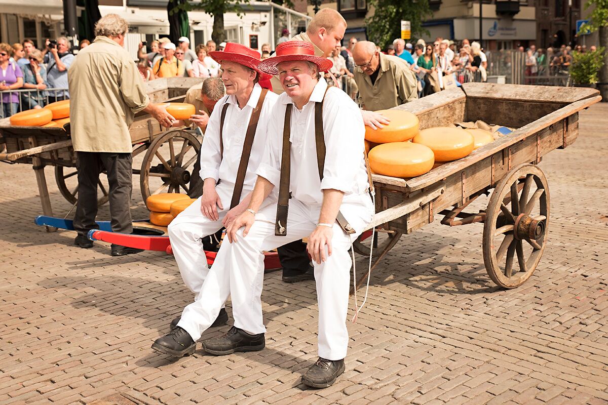 A group of people in traditional attire sitting on a wooden cart with cheese wheels.