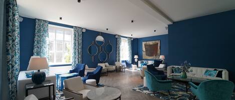Un salon spacieux aux couleurs bleu et blanc, comprenant un canapé, des fauteuils, une table basse et un tapis à motifs.