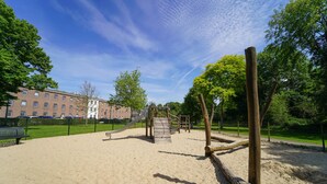A playground with a slide and climbing structures, surrounded by a fence and trees. - Fletcher Hotel-Restaurant De Oude Gevangenis - Alkmaar (Alkmaar)