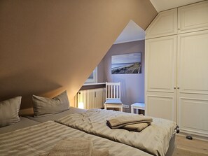 A bedroom with a sloped ceiling, a bed with striped bedding, a chair, and a wardrobe.