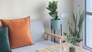 Een gezellige woonkamer met een bank, kussens, een hanglamp en potplanten.