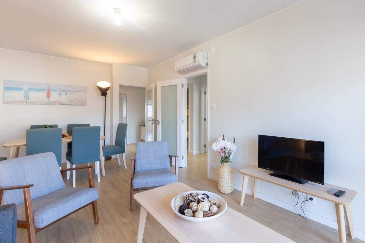 Ein modernes Wohnzimmer mit Flachbildfernseher, einem Essbereich mit blauen Stühlen und einem kleinen Tisch mit Dekoration.