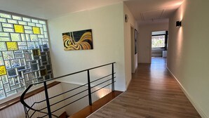 Un couloir doté d’un plancher en bois, d’un escalier avec une rampe noire et d’un mur orné d’une mosaïque et d’un tableau.