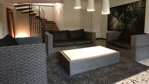 Un salon moderne avec un canapé, deux fauteuils, une table basse et un escalier en arrière-plan.