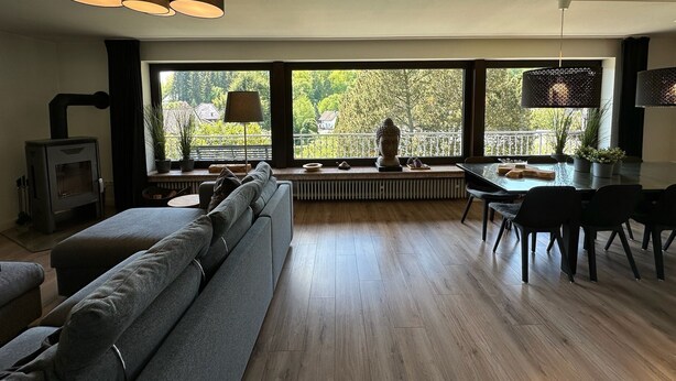 Un salon moderne comprenant un canapé, une table à manger et des chaises, de grandes fenêtres offrant une belle vue et un poêle à bois.