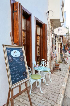 Un menú en pizarra frente a una cafetería, con una puerta de madera y contraventanas.