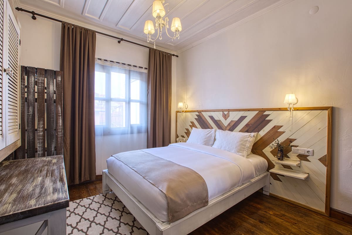 A neatly arranged hotel room with a large bed, bedside tables, a desk, and a window with curtains.