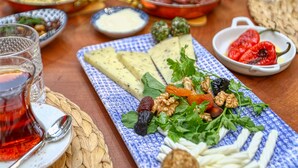 A table set with various dishes, including a plate of cheese, nuts, and vegetables, and a glass of red beverage. - Trilye Bay C Konak (Mudanya)