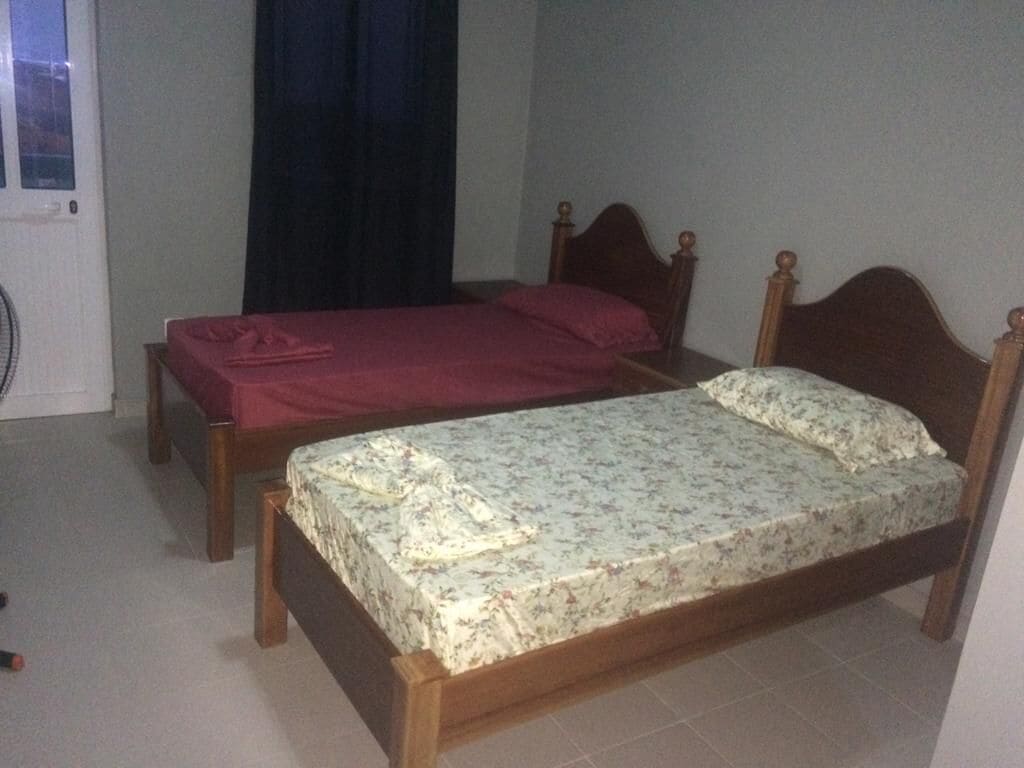 A room with two wooden beds, one with a floral bedspread and the other with a solid color bedspread.