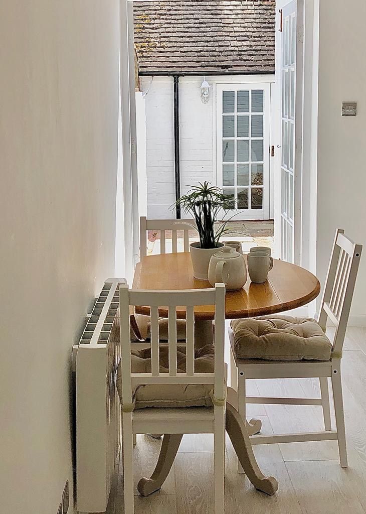 A dining area with a wooden table and white chairs, a potted plant, and a view of the outside.