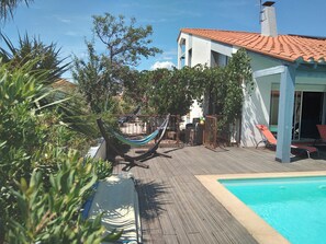 Une terrasse en bois avec une piscine, un hamac et un bâtiment doté d’un toit en tuiles.