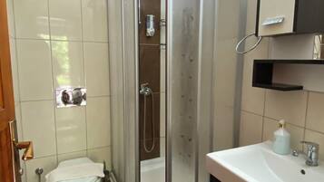 A bathroom with a glass-enclosed shower, a toilet, and a sink with a mirror above.