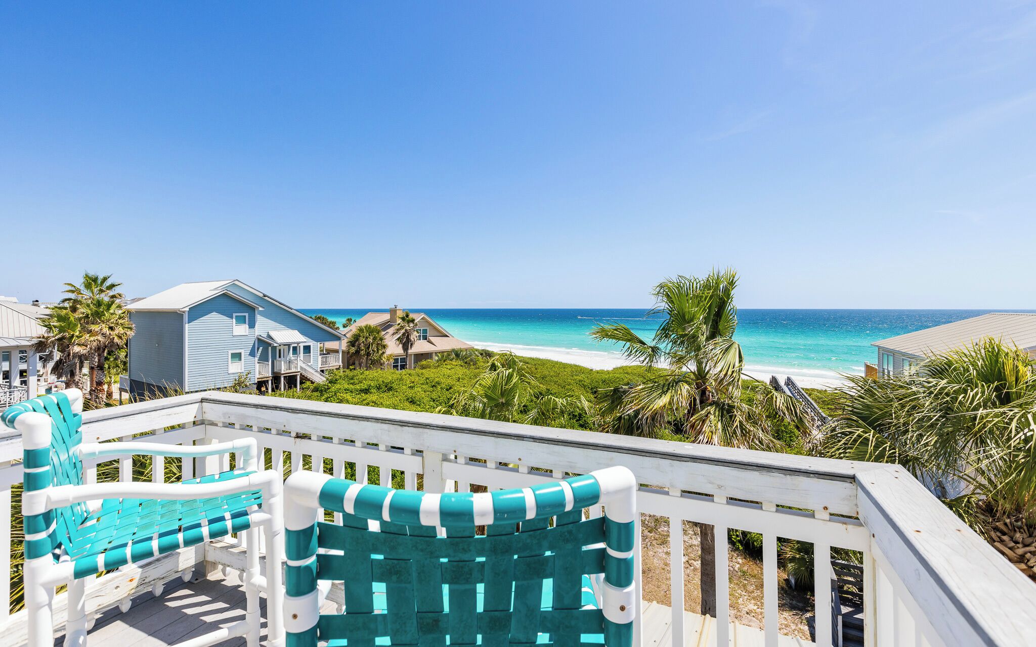 A beachfront property with a pool area, a white fence, and a view of the ocean.