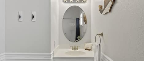A bathroom with a white vanity, a round mirror, and a lighted vanity mirror.