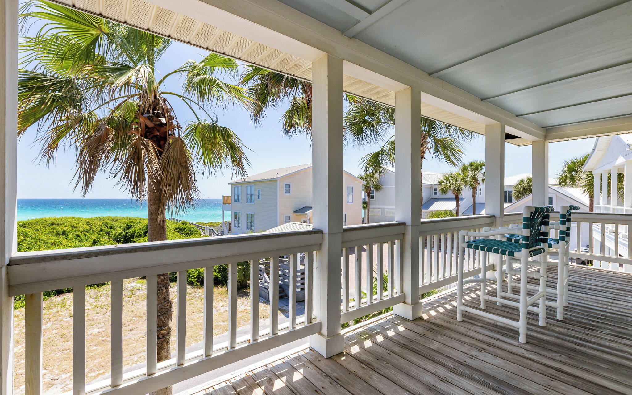 A covered porch with a view of the ocean and palm trees.