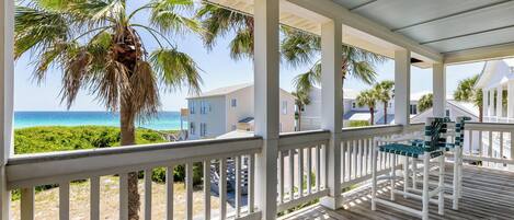 A covered porch with a view of the ocean and palm trees.