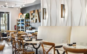 A modern restaurant interior with wooden chairs, round tables, and a white cushioned bench. - Seagrove Beach, Gated Neighborhood, Pool! (Santa Rosa Beach)
