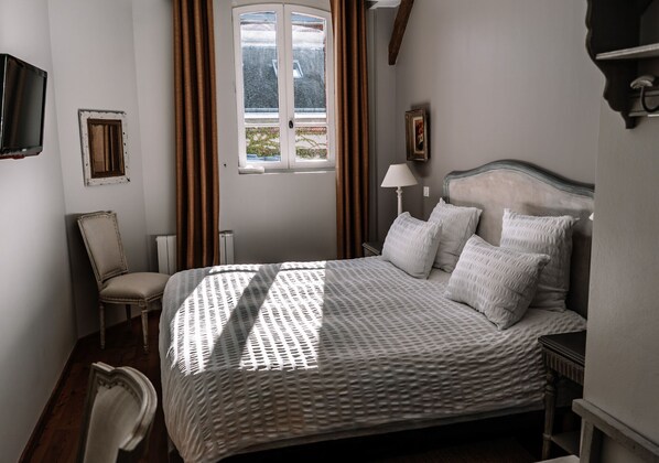 Un dormitorio ordenado con cama, silla, lámpara y ventana con cortinas.