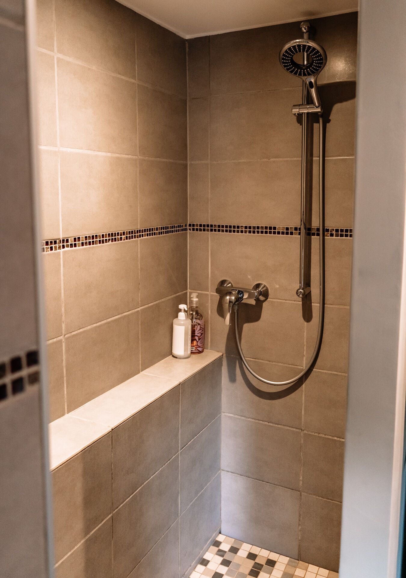 A shower area with a handheld showerhead, a wall-mounted faucet, and a shelf with toiletries.