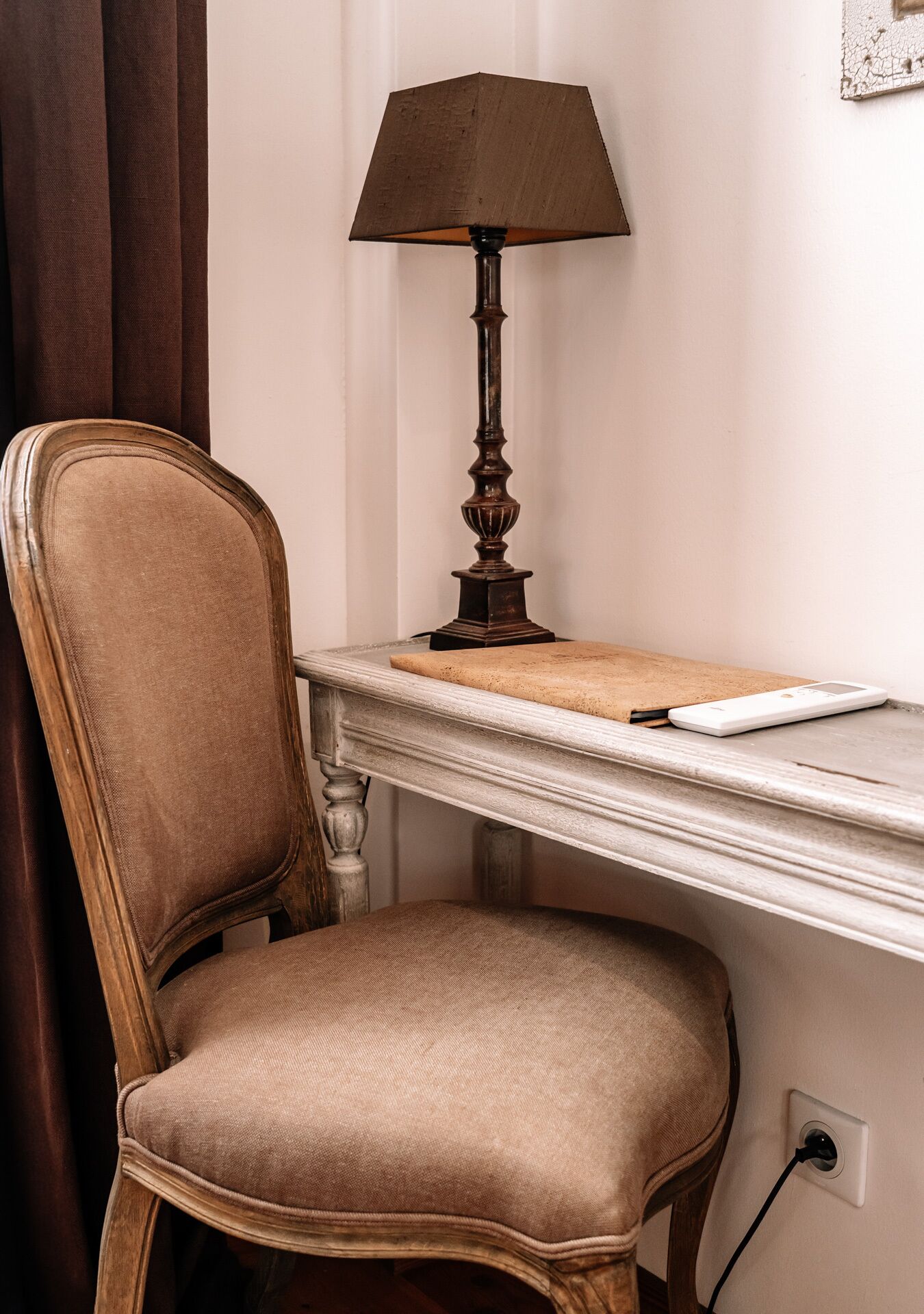 A wooden chair with a cushioned seat and back, a table with a lamp, and a wall socket.