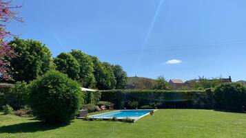 Ein Garten mit Schwimmbecken, umgeben von üppigem Grün und blauem Himmel.