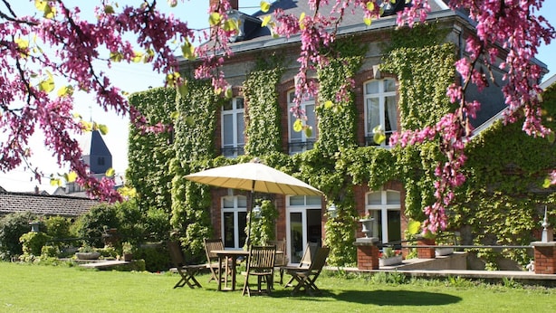 A building with ivy-covered walls, a patio with a table and chairs, and a clear sky.
