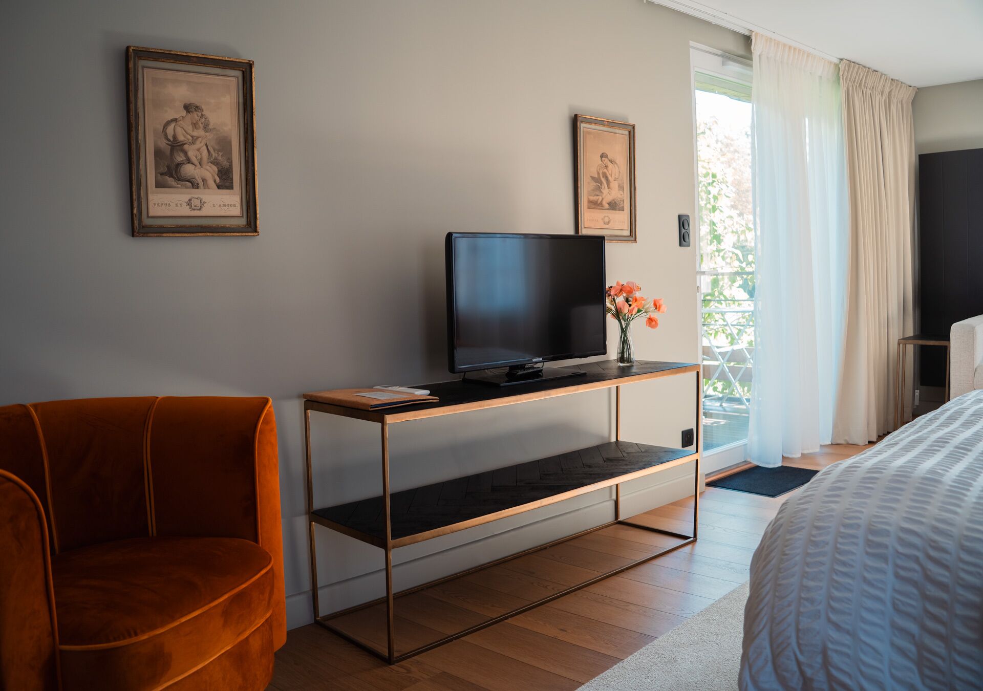 Una habitación de hotel moderna con una cama, un televisor sobre un mueble de madera, una silla y dos cuadros en la pared.
