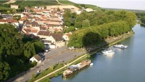 A riverside town with residential buildings, a marina with boats, and a pedestrian pathway along the river.