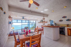 A spacious kitchen with a large island, wooden chairs, and a view of the sea.