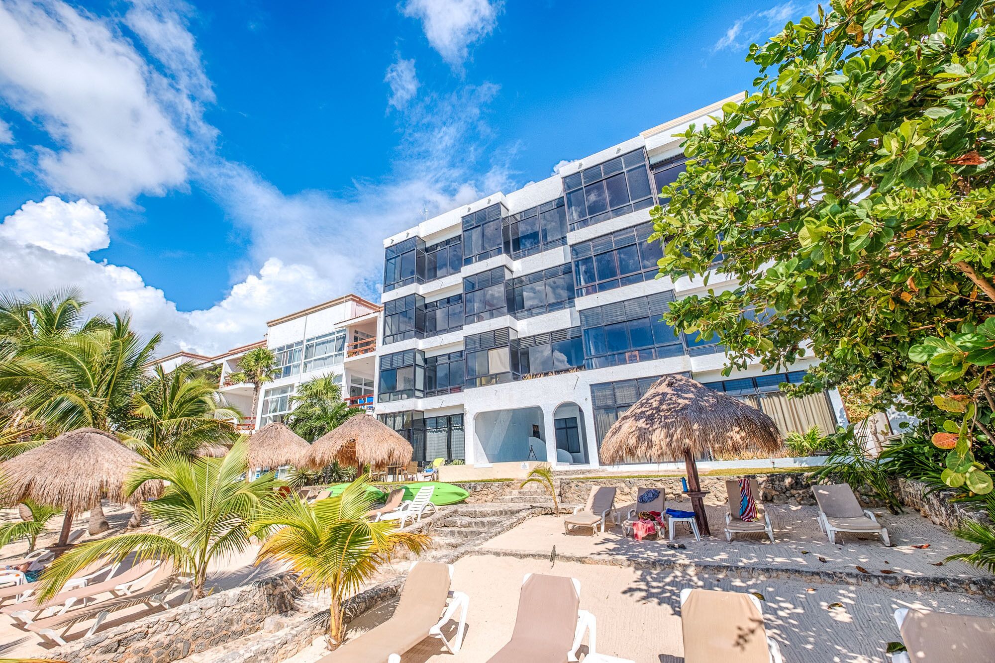 Un hôtel moderne à plusieurs étages, situé en bord de mer, et doté d’un espace piscine avec des chaises longues.