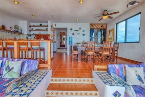 Amplia sala de estar con mesa de comedor, sillas de madera y un sofá con cojines estampados.