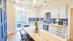 A modern kitchen with white cabinets, a wooden dining table, and a potted plant. - Host & Stay | Simba House (Saltburn-by-the-Sea)