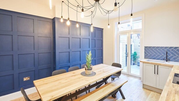 A modern kitchen with a wooden table, blue panel walls, and a view to the outside. - Host & Stay | Simba House (Saltburn-by-the-Sea)