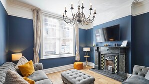 A living room with a grey sofa, ottoman, and a fireplace with a TV above it. - Host & Stay | Simba House (Saltburn-by-the-Sea)