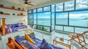 A spacious room with a large window offering a view of the ocean, a ceiling fan, and a wooden chair. - Perfect for a couple to enjoy the breathtaking views of the Caribbean! (Akumal)