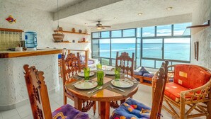 A dining area with a view of the ocean, featuring a round wooden table, chairs, and a large window. - Perfect for a couple to enjoy the breathtaking views of the Caribbean! (Akumal)
