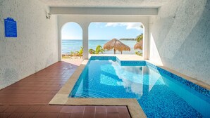 A swimming pool with a view of the ocean, a beach, and a thatched umbrella. - Perfect for a couple to enjoy the breathtaking views of the Caribbean! (Akumal)