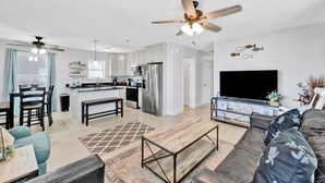 A modern kitchen with a central island, a dining area with chairs, a sofa, and a TV.