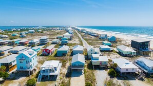 A coastal residential area with multiple houses, some elevated on stilts, and a beach in the background.