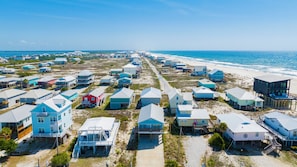 A coastal residential area with multiple houses, some elevated on stilts, and a beach in the background.