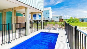 A swimming pool with a wooden deck, a fenced area, and a view of houses in the background.