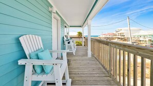 A wooden deck with white Adirondack chairs and a view of buildings in the distance.