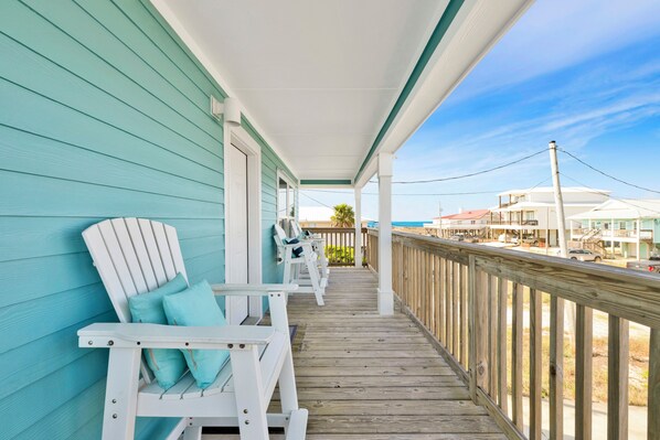 A wooden deck with white Adirondack chairs and a view of buildings in the distance.