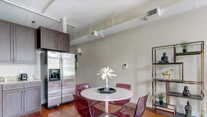 A modern kitchen with stainless steel appliances, a dining area with a round table and red chairs, and a decorative shelf with figurines. - The Loft on Broughton, Modern | Stylish | Chic (Savannah)