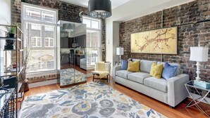 A living room with a brick wall, a sofa, a coffee table, a rug, and a large mirror. - The Loft on Broughton, Modern | Stylish | Chic (Savannah)