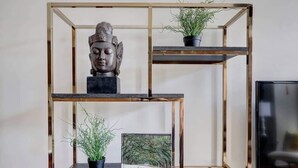 A three-tiered metal shelf unit with a Buddha head sculpture on the top tier, two potted plants on the middle and bottom tiers, and a framed picture with the word 'SAVANNAH' on the bottom tier. - The Loft on Broughton, Modern | Stylish | Chic (Savannah)